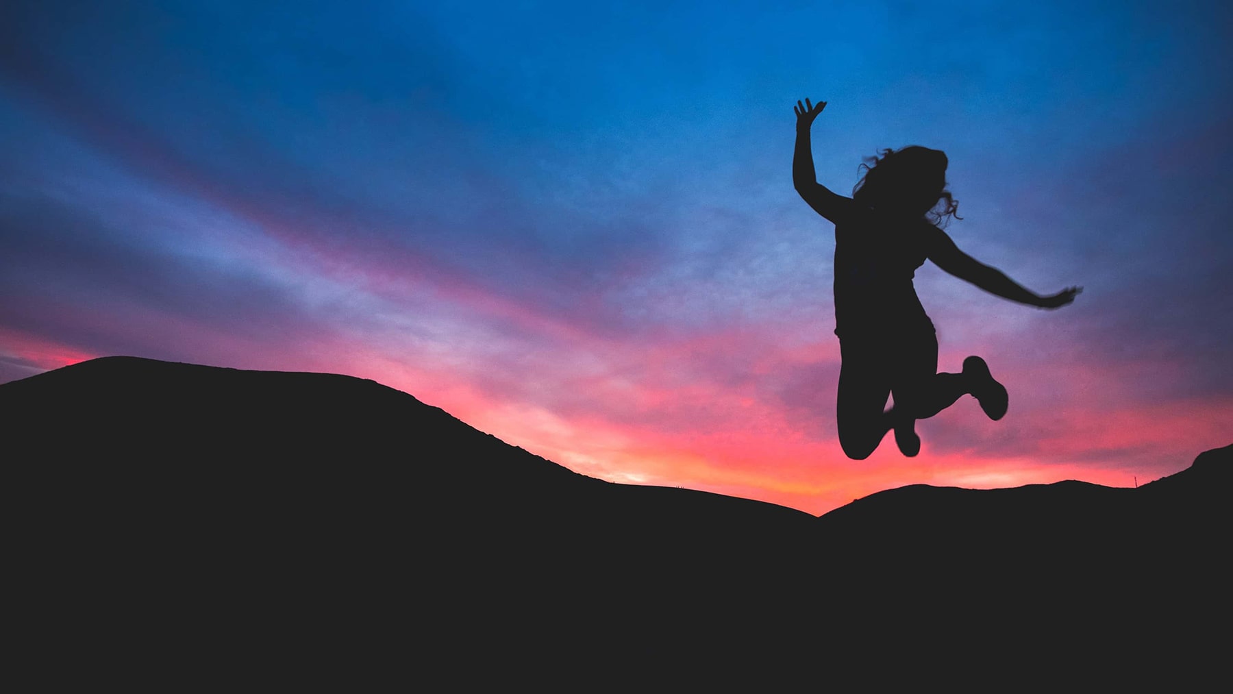 female jumping in front of sunset