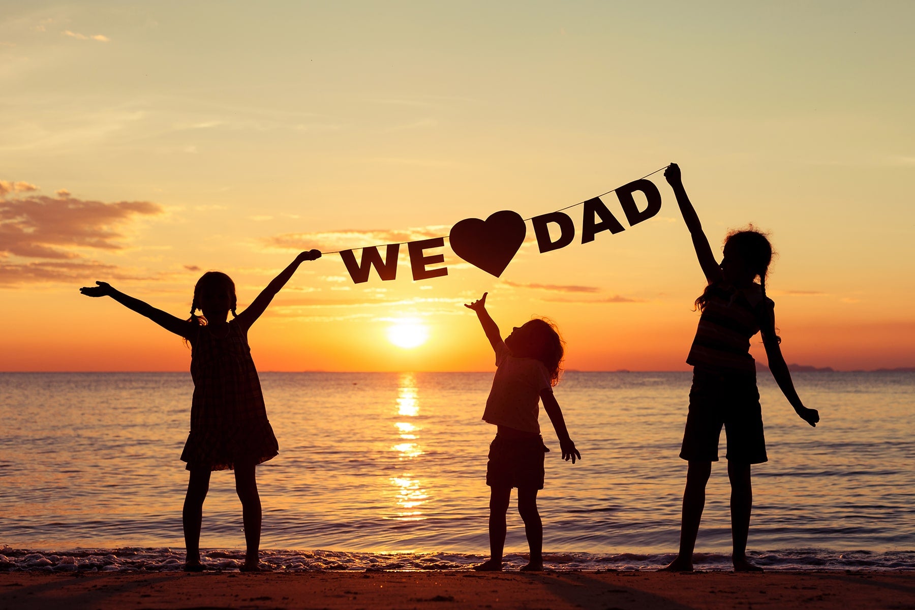 Children holding we love dad sign on beach in front of sunset